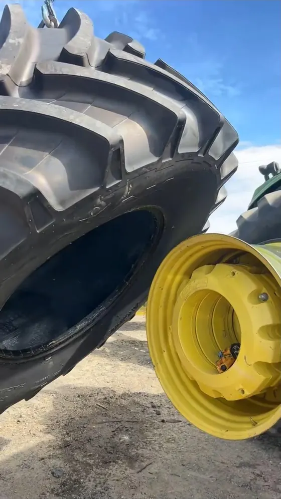 Agricultural tire lifted by hoist next to a yellow tractor rim on the ground